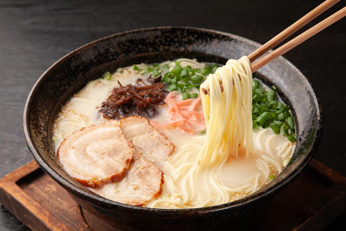 Creamy tonkotsu ramen with chashu pork, noodles lifted by wooden chopsticks